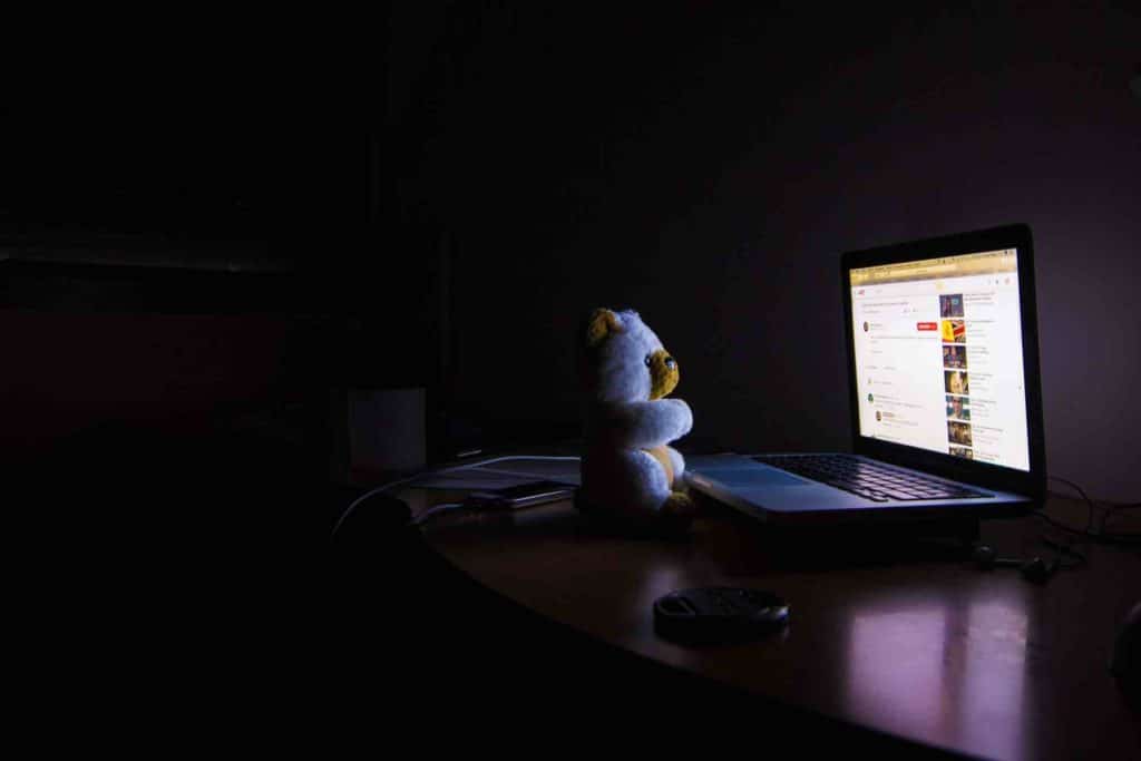 Picture of a teddy bear with insomnia, sitting in the dark in front of a bright laptop