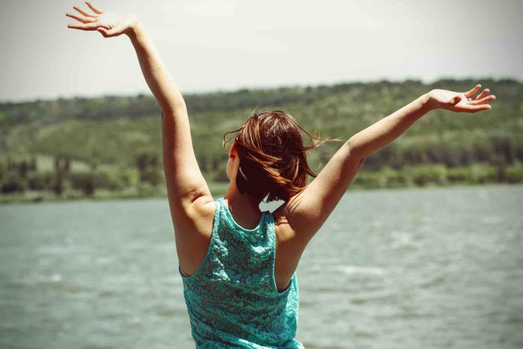Happy woman with her arms in the air, facing a body of water