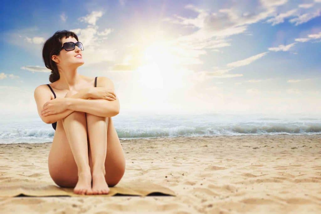 Woman with nice skin sitting on a sunny beach with sunglasses on