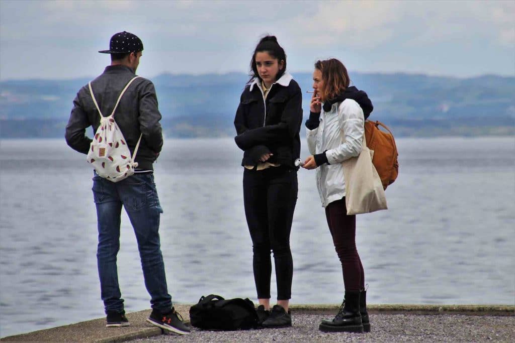 Three young adults smoking cigarettes by a lake