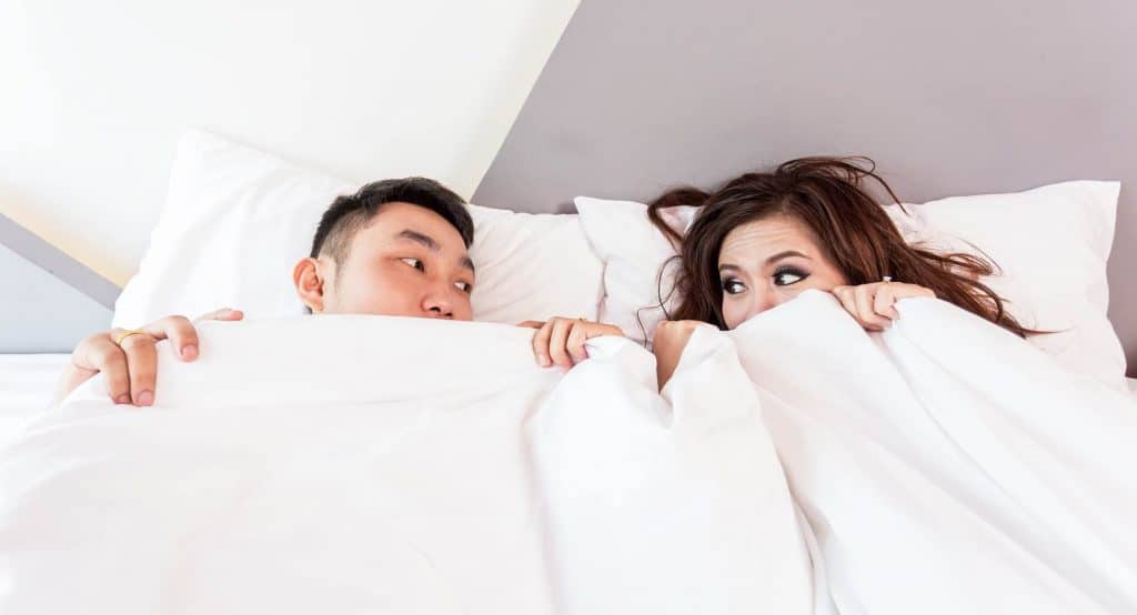 A man and woman looking at each other under the bed covers