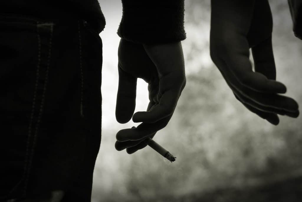 Black and white photo of two people's hands, one holding a cigarette