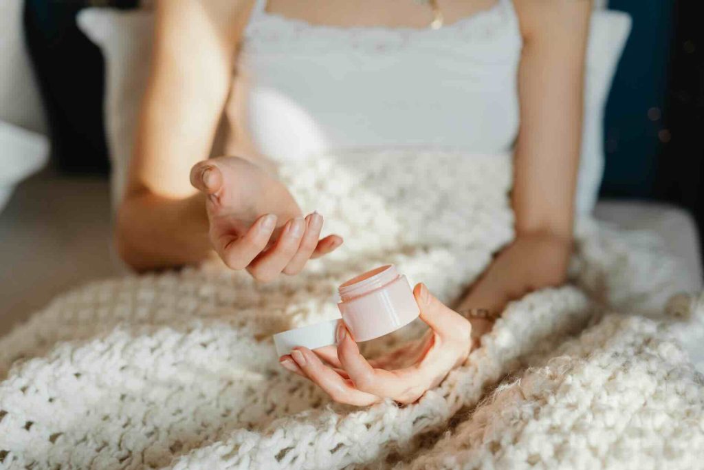 Woman sitting in bed with a blanket applying skincare cream