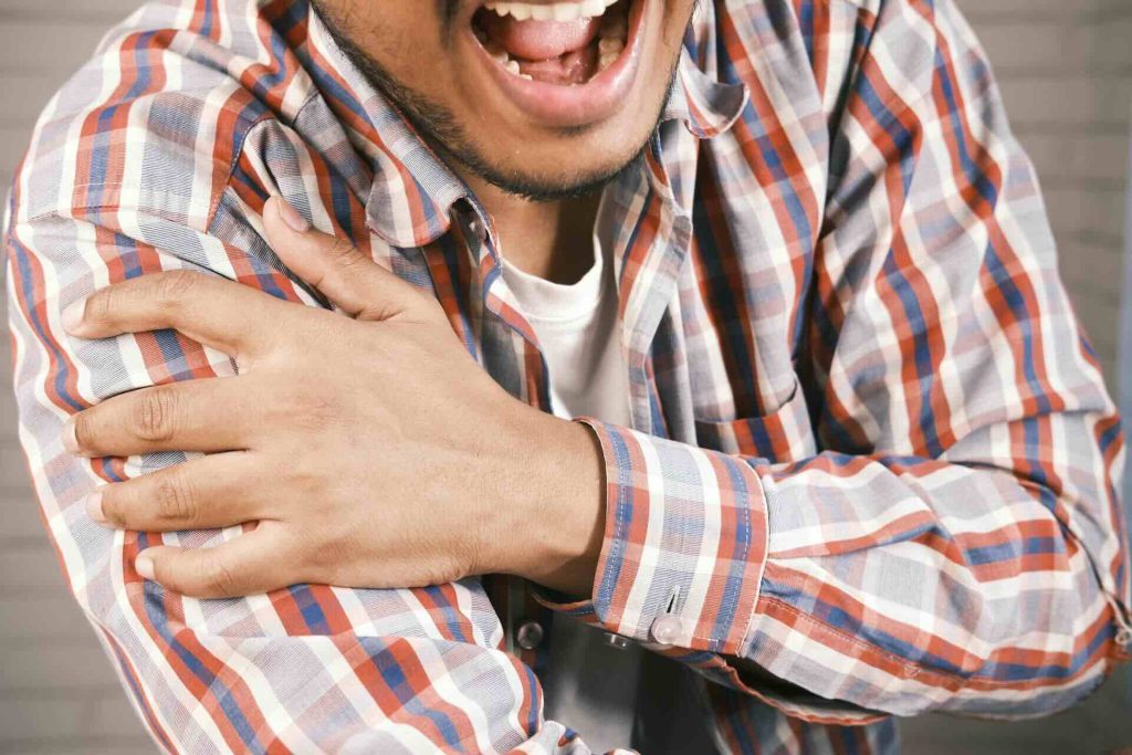Man wincing while holding the front of his right shoulder